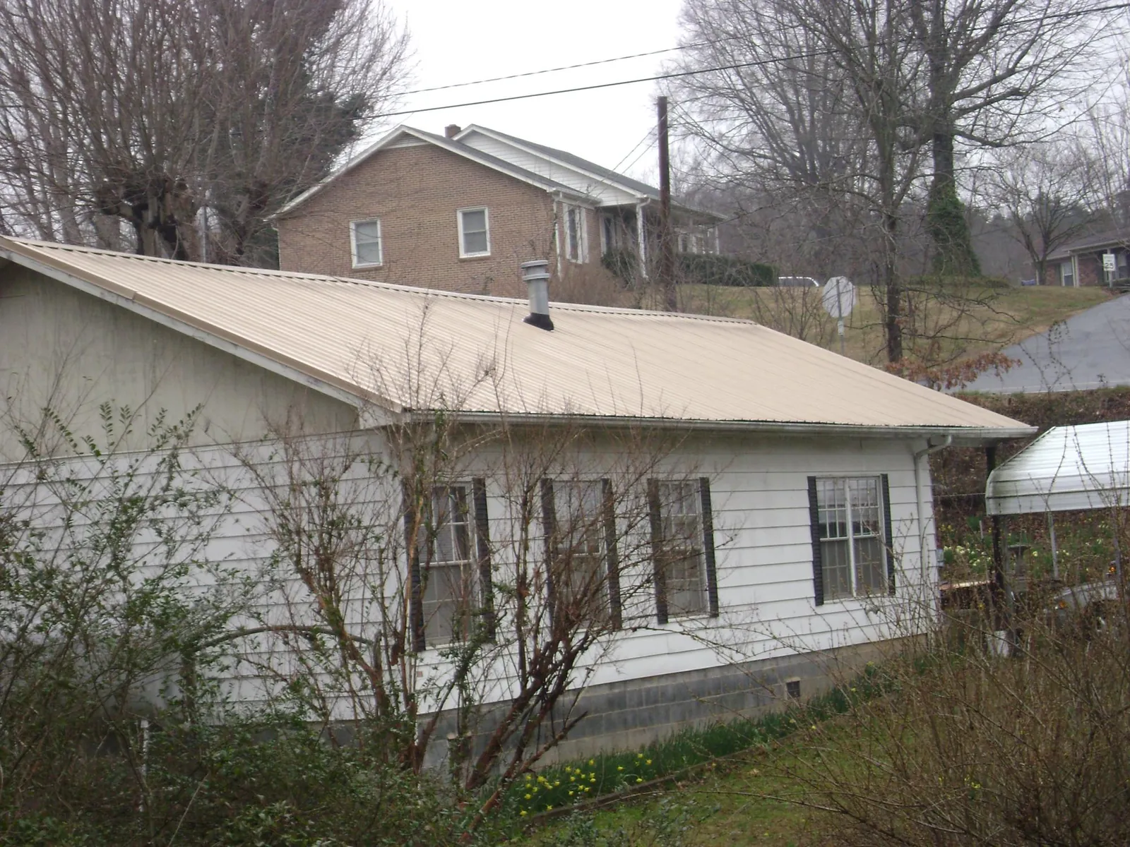 Tan metal roof on a white sided house set into a hillside — Commercial Roofing by Roofing Brothers in Ponte Vedra